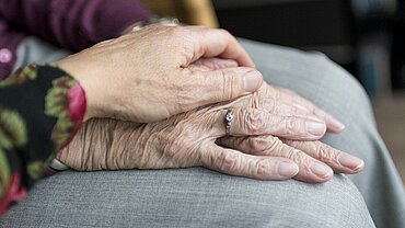 Eine Hand hält die Hände einer alten Frau. 