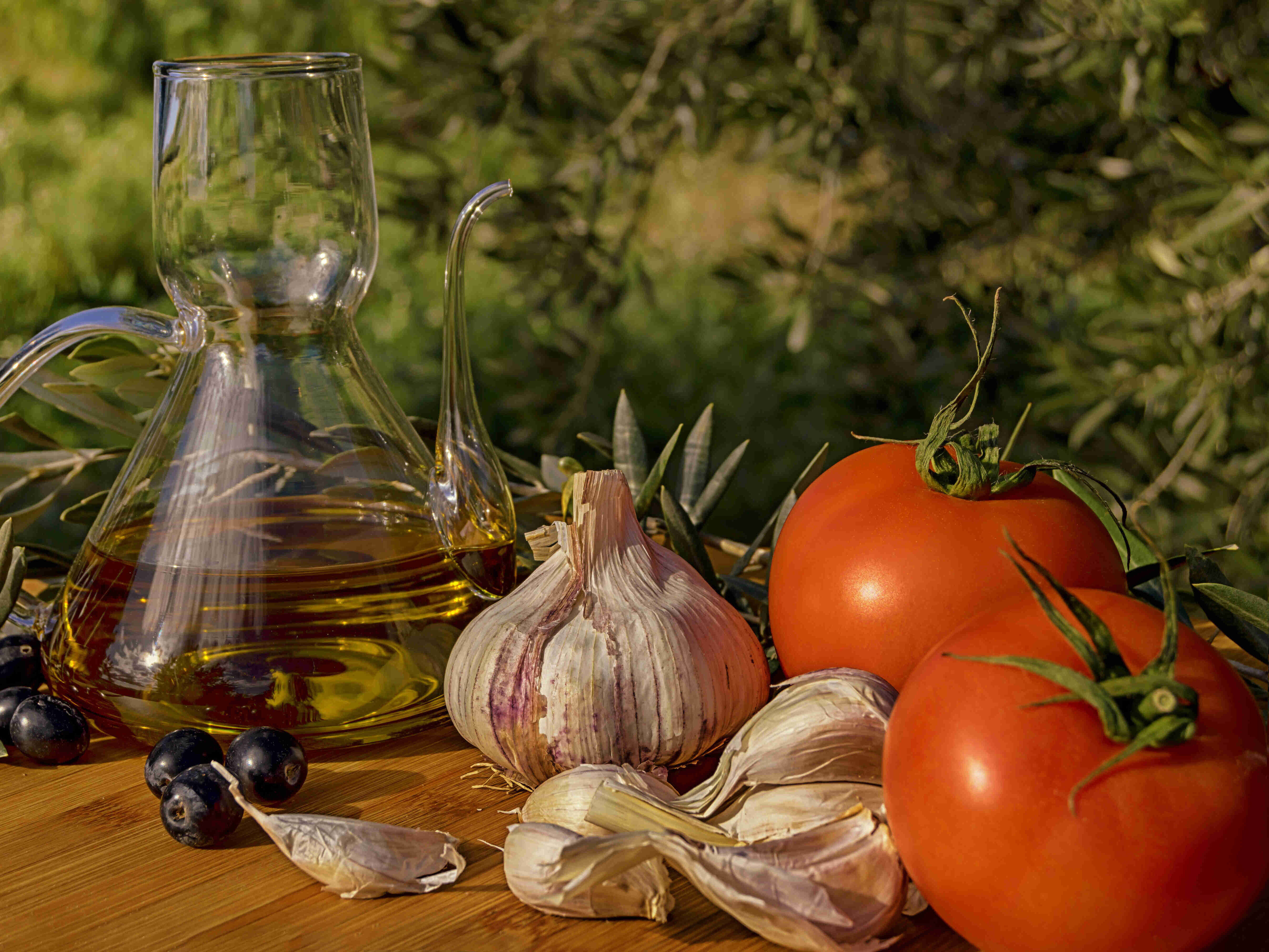 Knoblauch, Tomaten und eine Karaffe mit Olivenöl auf einem Tisch.