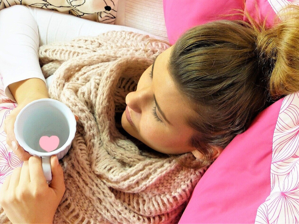 Eine Frau liegt mit einem Schal im Bett.