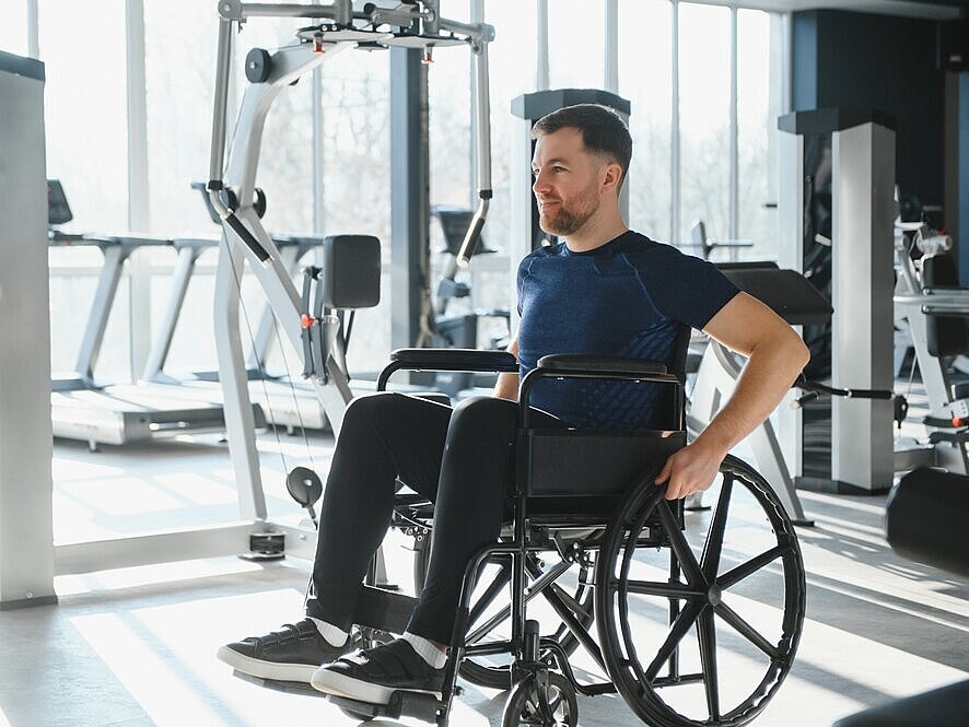 Ein Mann im Rollstuhl ist in einem Raum mit Trainingsgeräten.